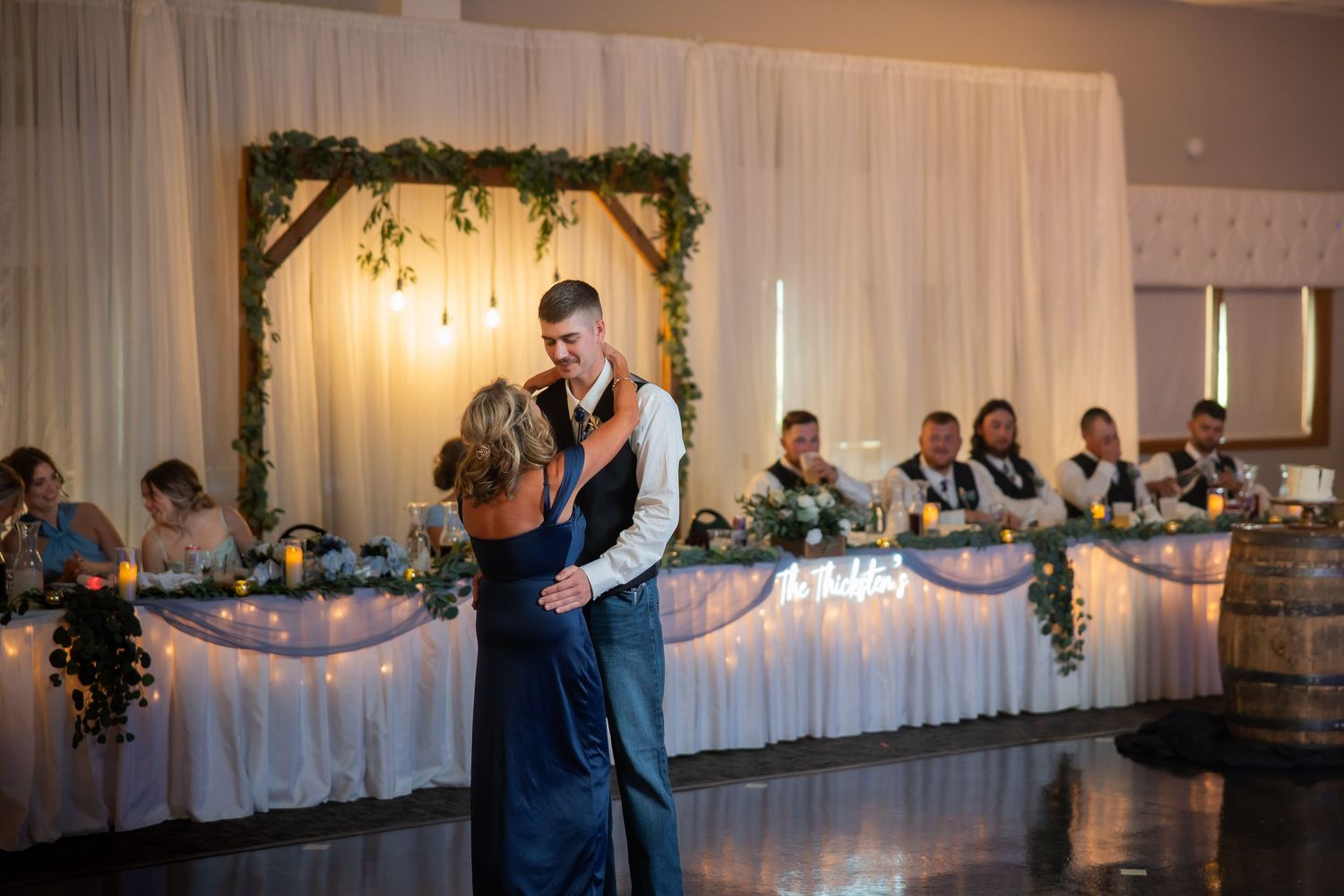 Couple shares an intimate dance in front of the elegant greenery arch at their wedding reception.
