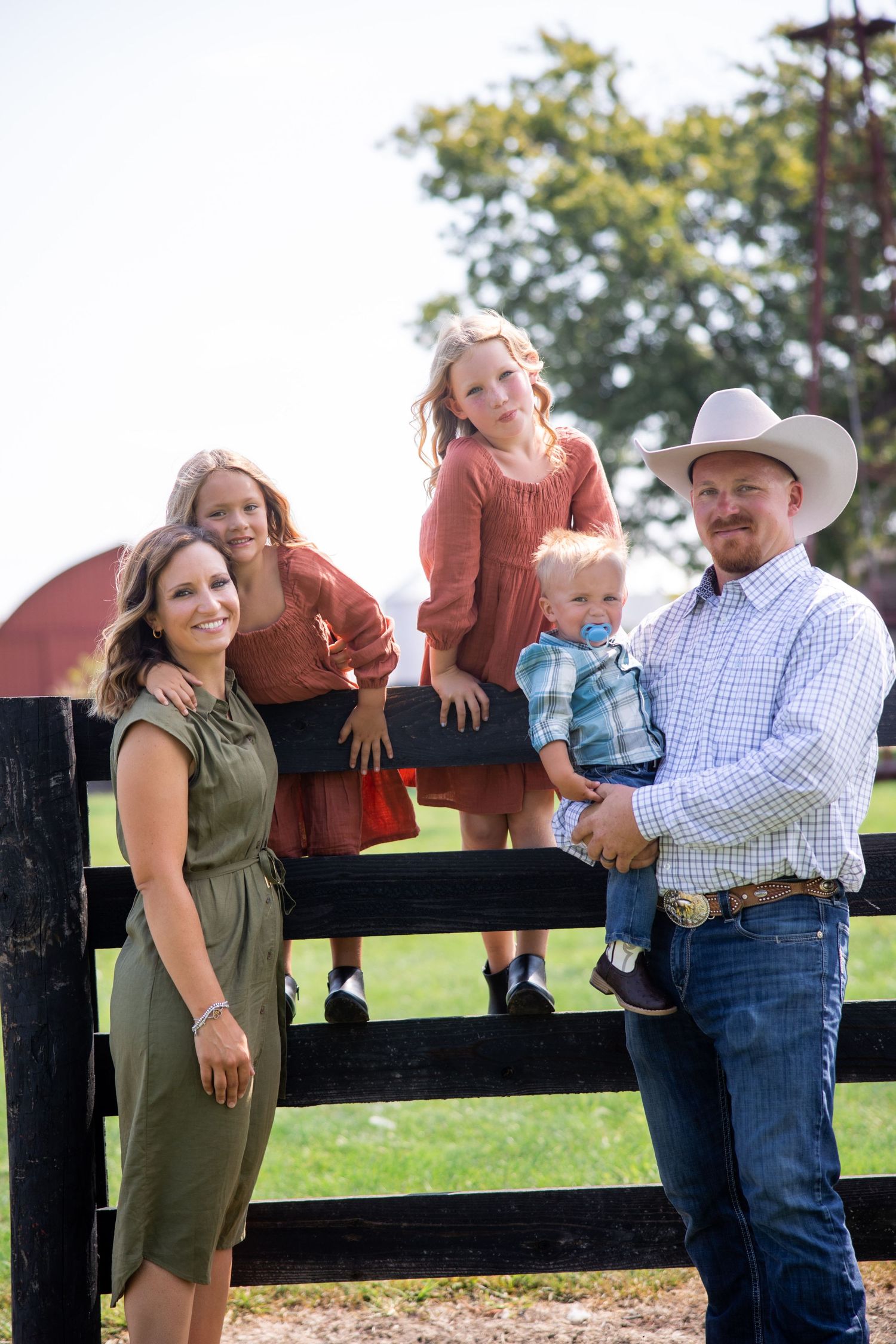 Family posing together by rustic wooden fence in countryside setting.