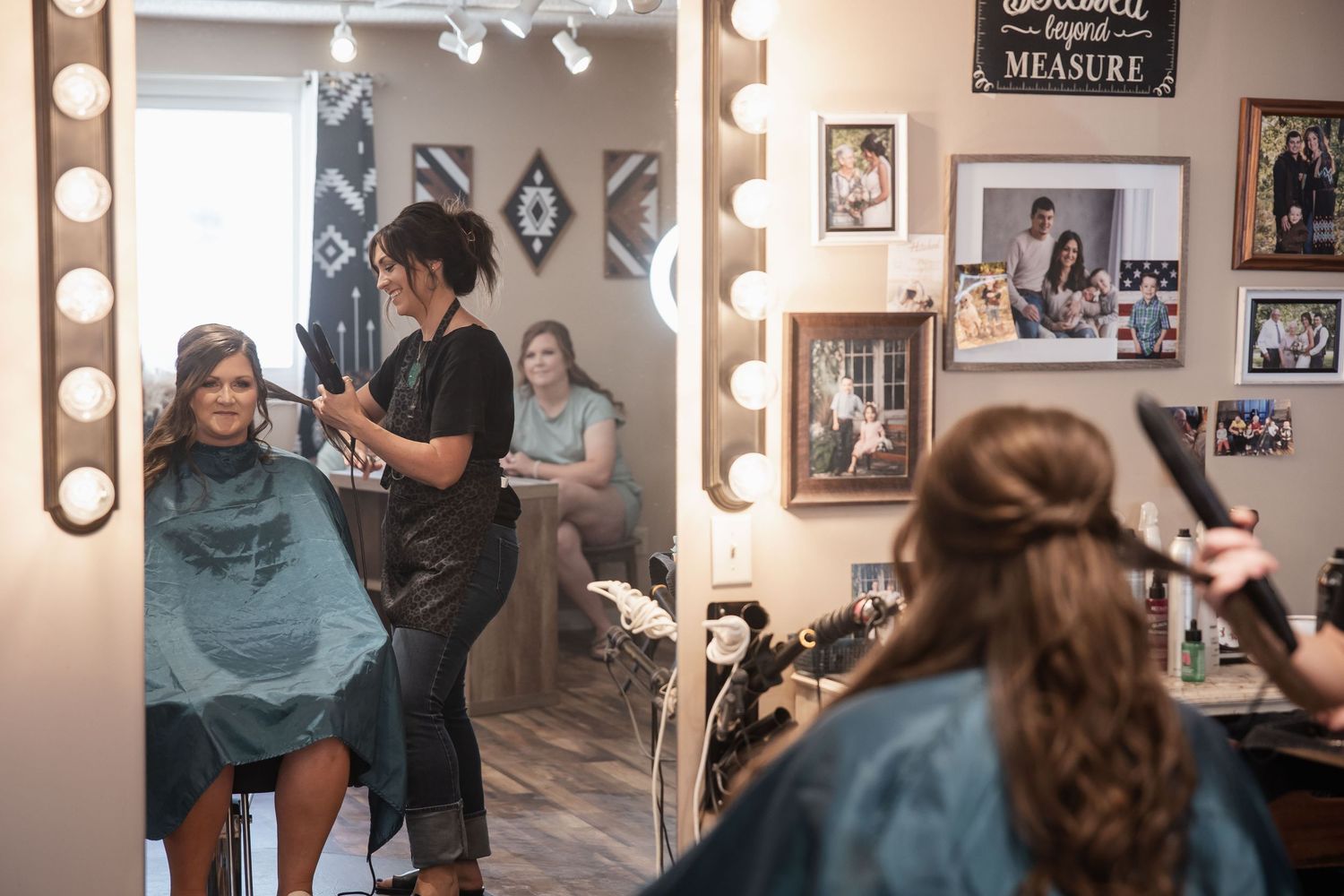 Bride getting hair styled in a salon mirror reflection with Hollywood lights and decorative wall art.