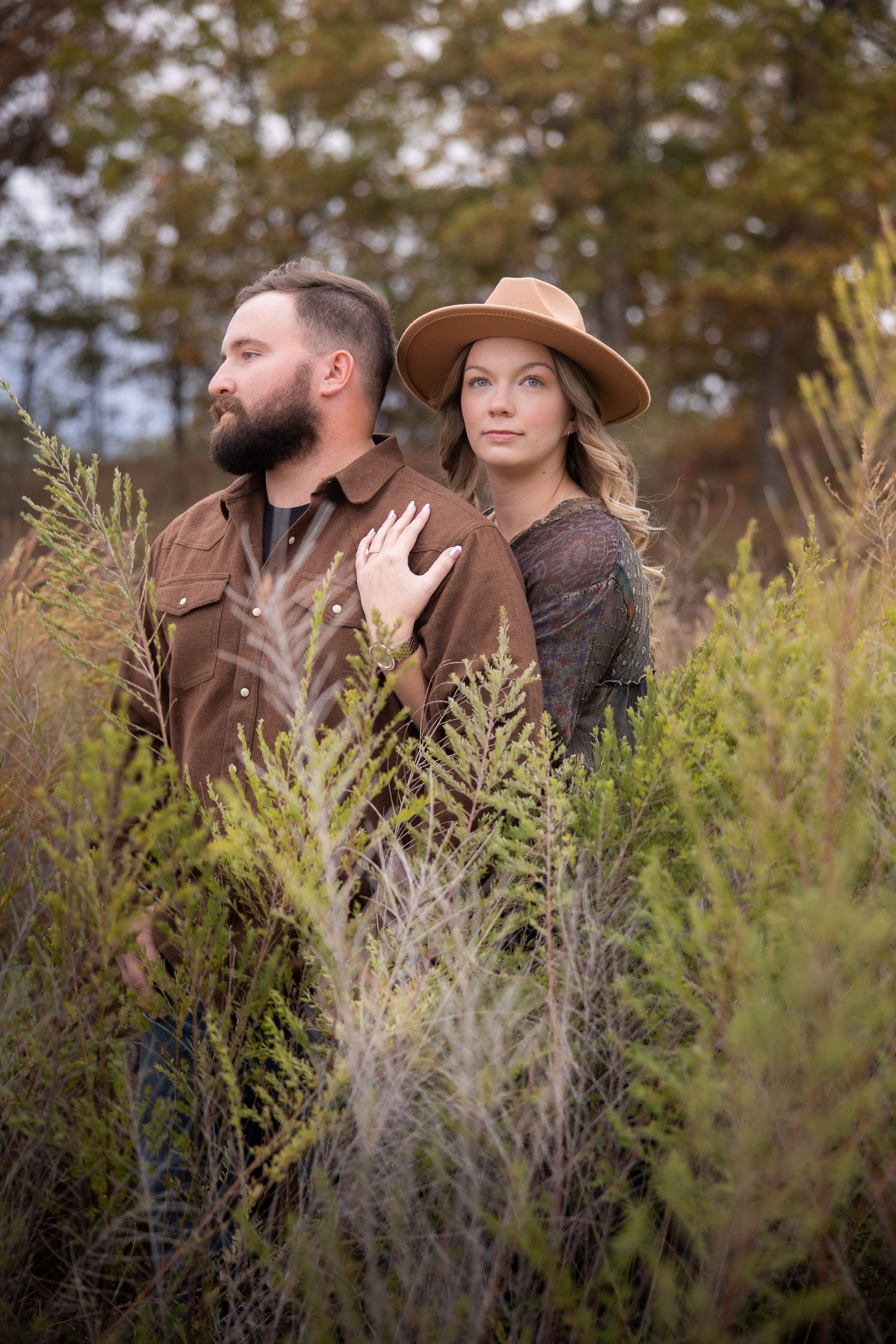 A couple in brown attire poses together among tall grasses during an autumn outdoor photoshoot.
