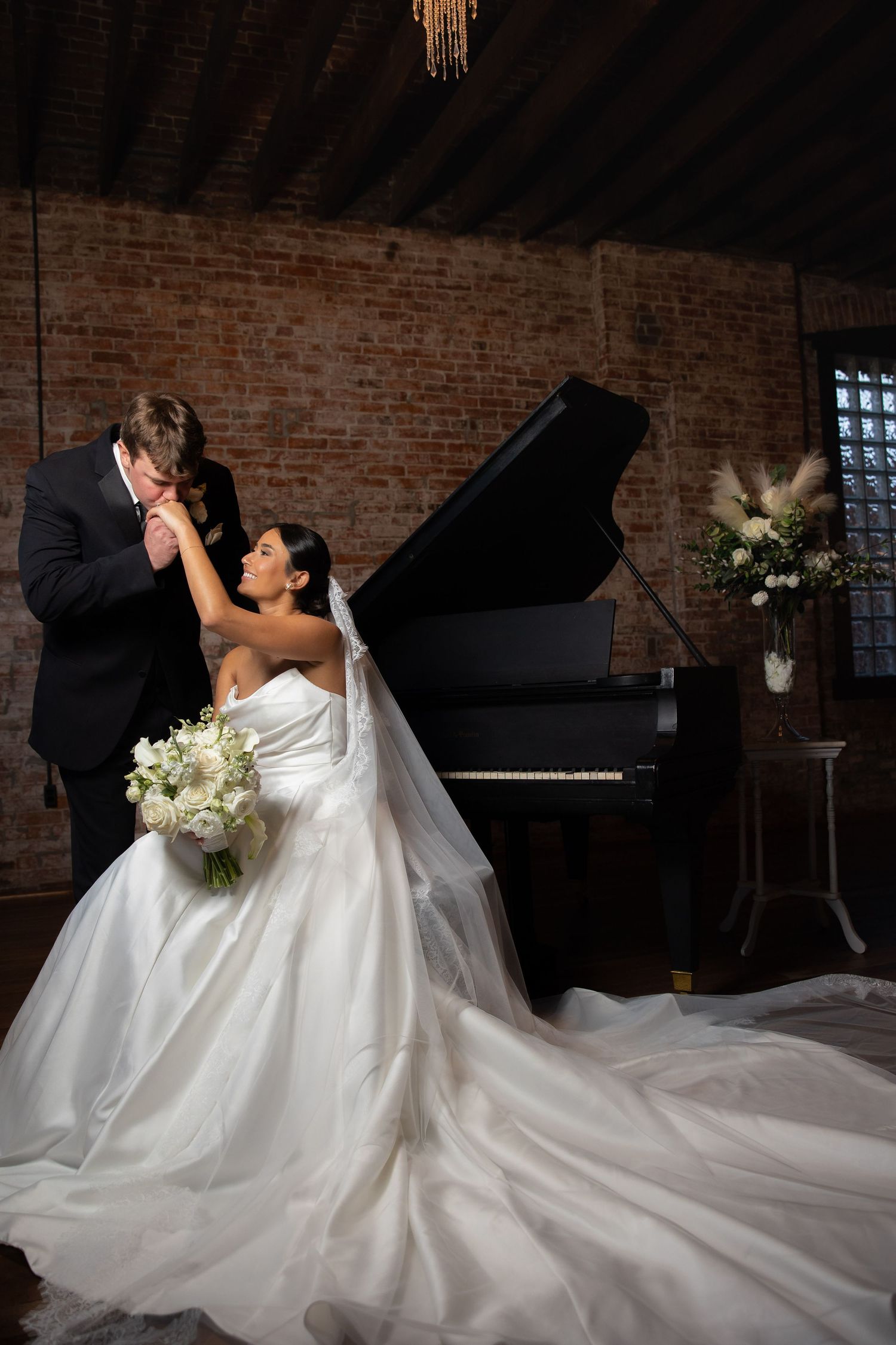 Romantic wedding couple dances in an industrial brick venue with a grand piano in the background.