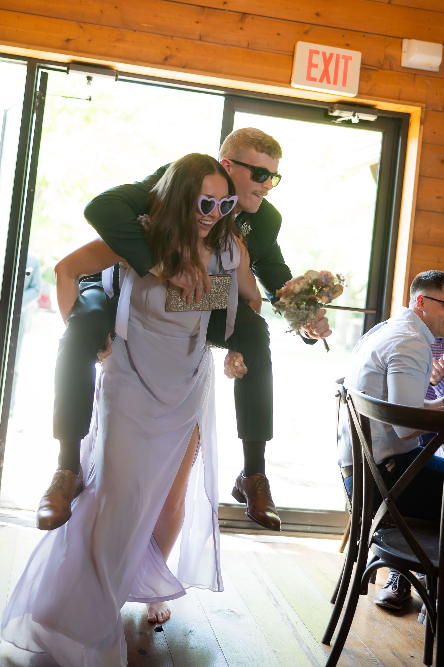 Bride and groom entering reception wearing fun heart sunglasses for a playful piggyback entrance.
