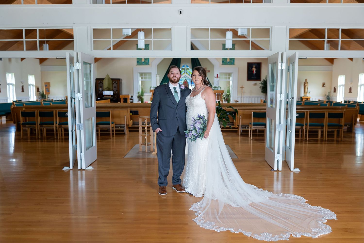 Bride and groom pose together in elegant wedding hall with hardwood floors and white columns.