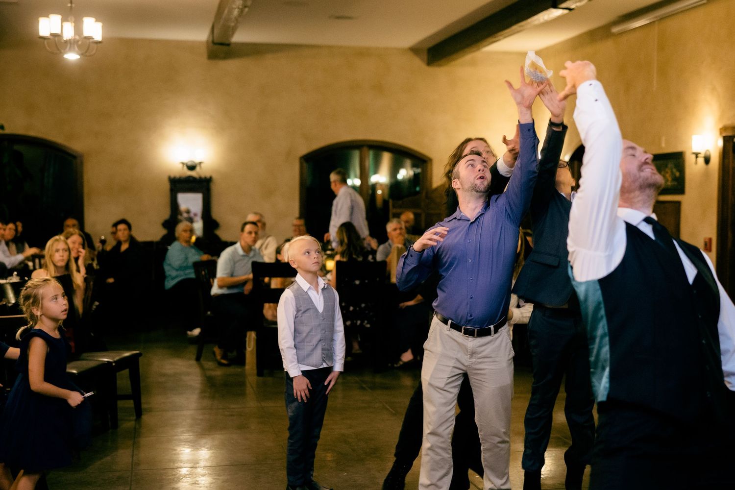 Guests dancing and celebrating at a wedding reception in a rustic venue with wooden beams.