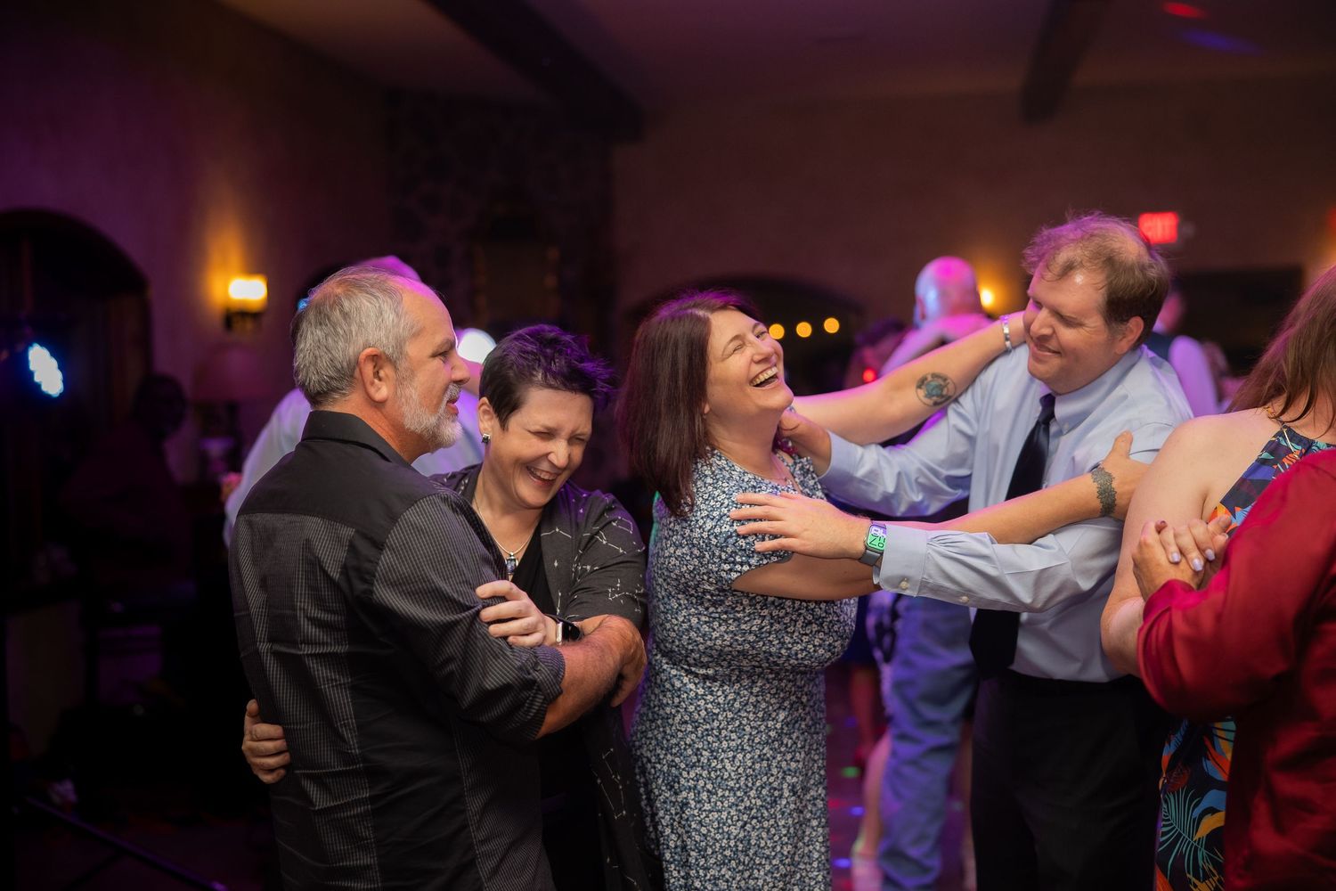 Wedding guests dancing together on dimly lit dance floor during reception.