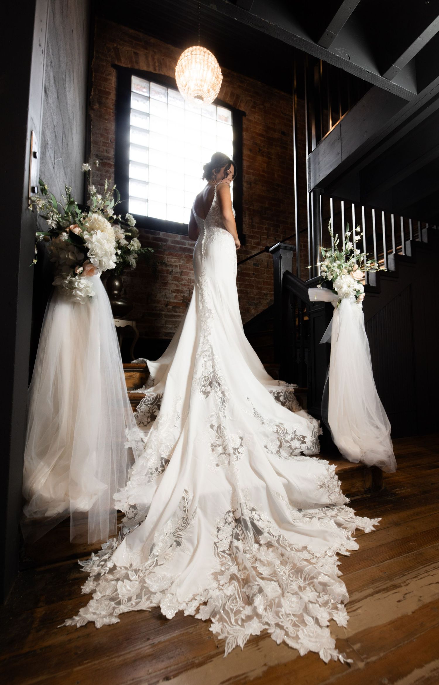 Elegant wedding dress with floral train displayed in a rustic brick venue.