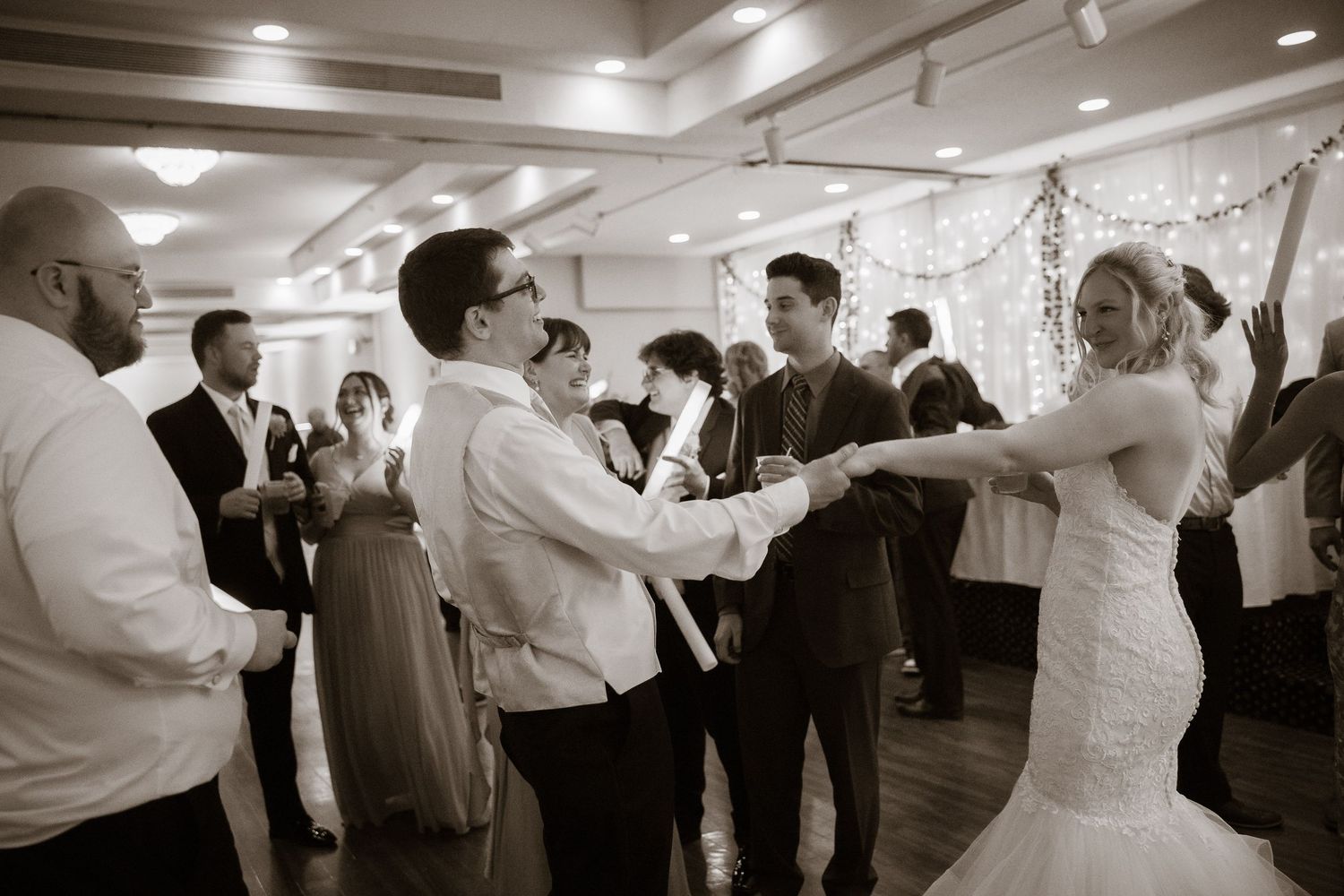 Wedding reception dance floor filled with guests celebrating under decorative lighting.