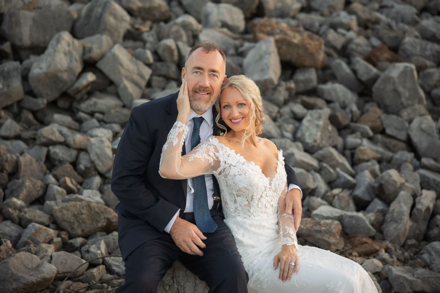 Couple sitting together on rocky shoreline during sunset wedding photoshoot.