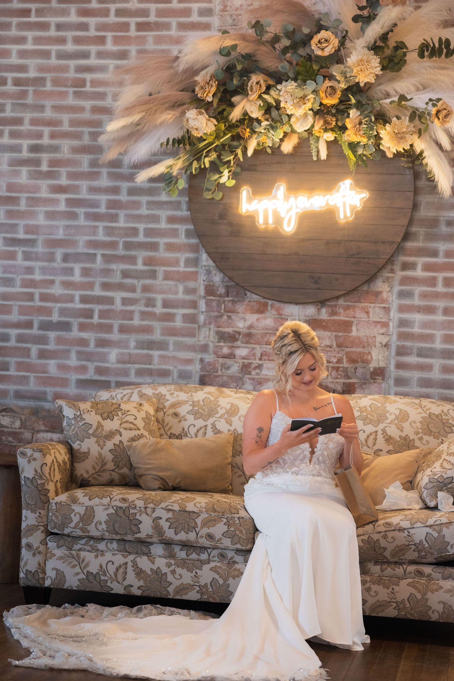 A bride in a white wedding dress reclines on a vintage floral couch beneath illuminated decor.