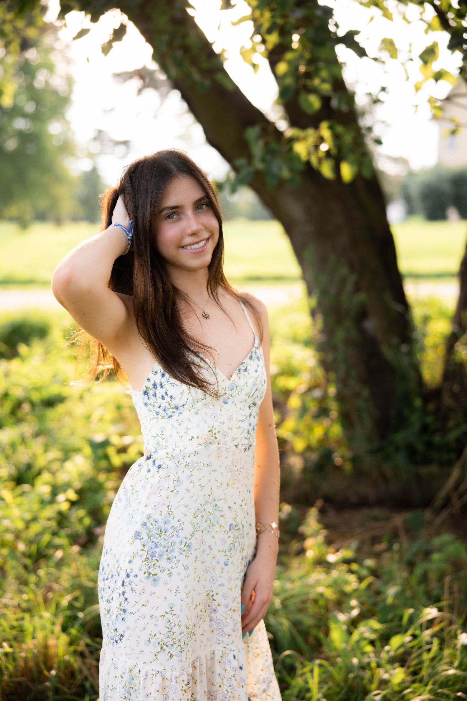 Person wearing a white lace dress poses playfully in a sunlit garden setting.