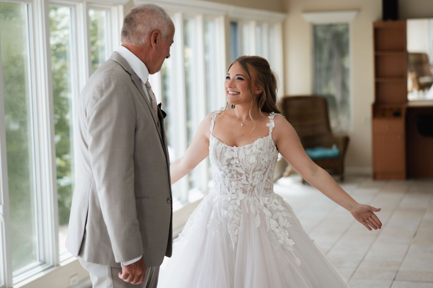 Bride in lace ballgown shares first look moment with father in sunlit room.