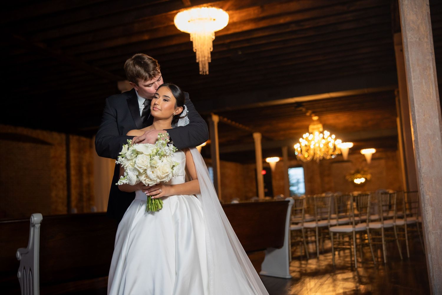 Romantic wedding dance in an industrial venue with chandeliers and brick walls.