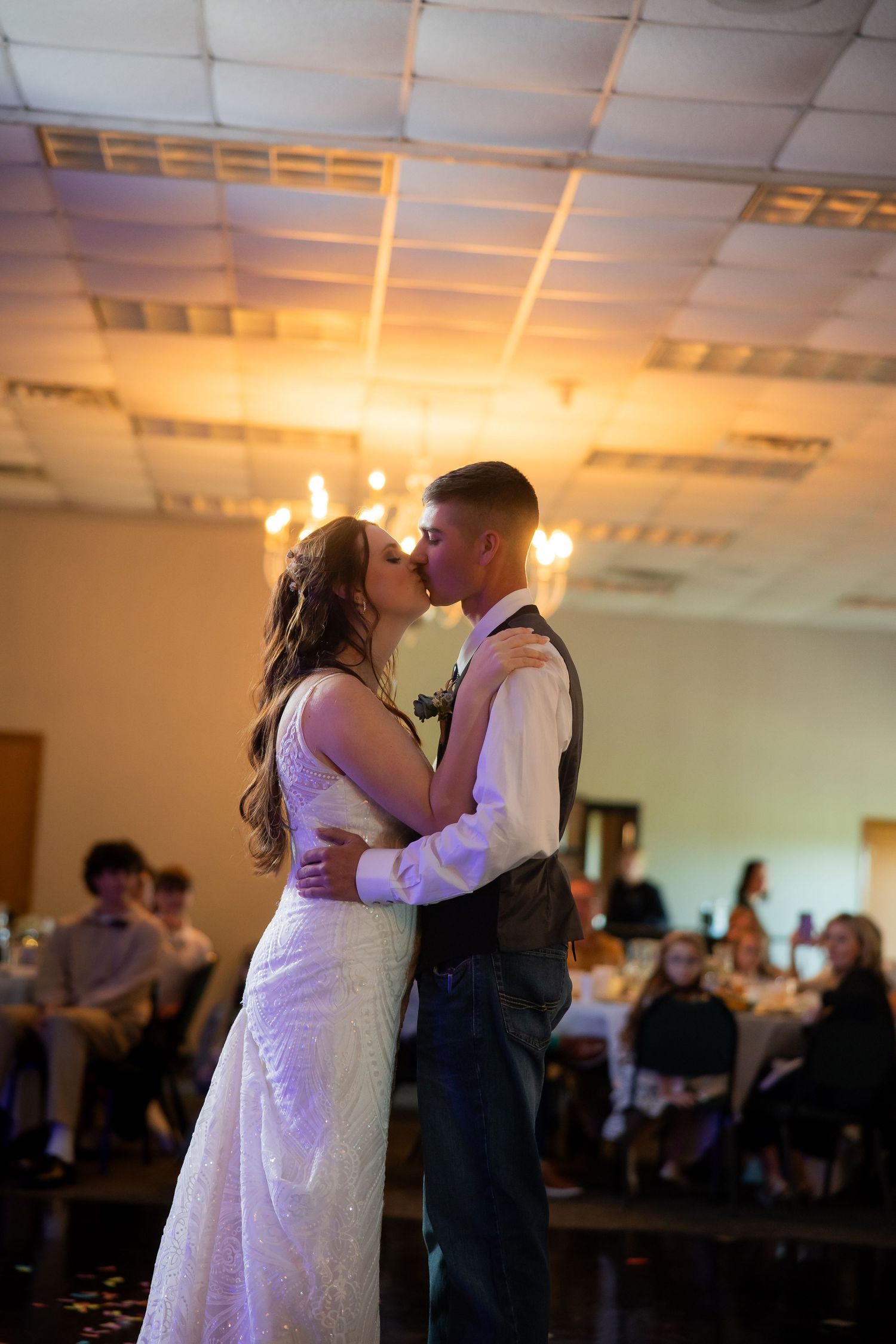 Bride and groom share romantic first dance kiss in warmly lit wedding reception hall.