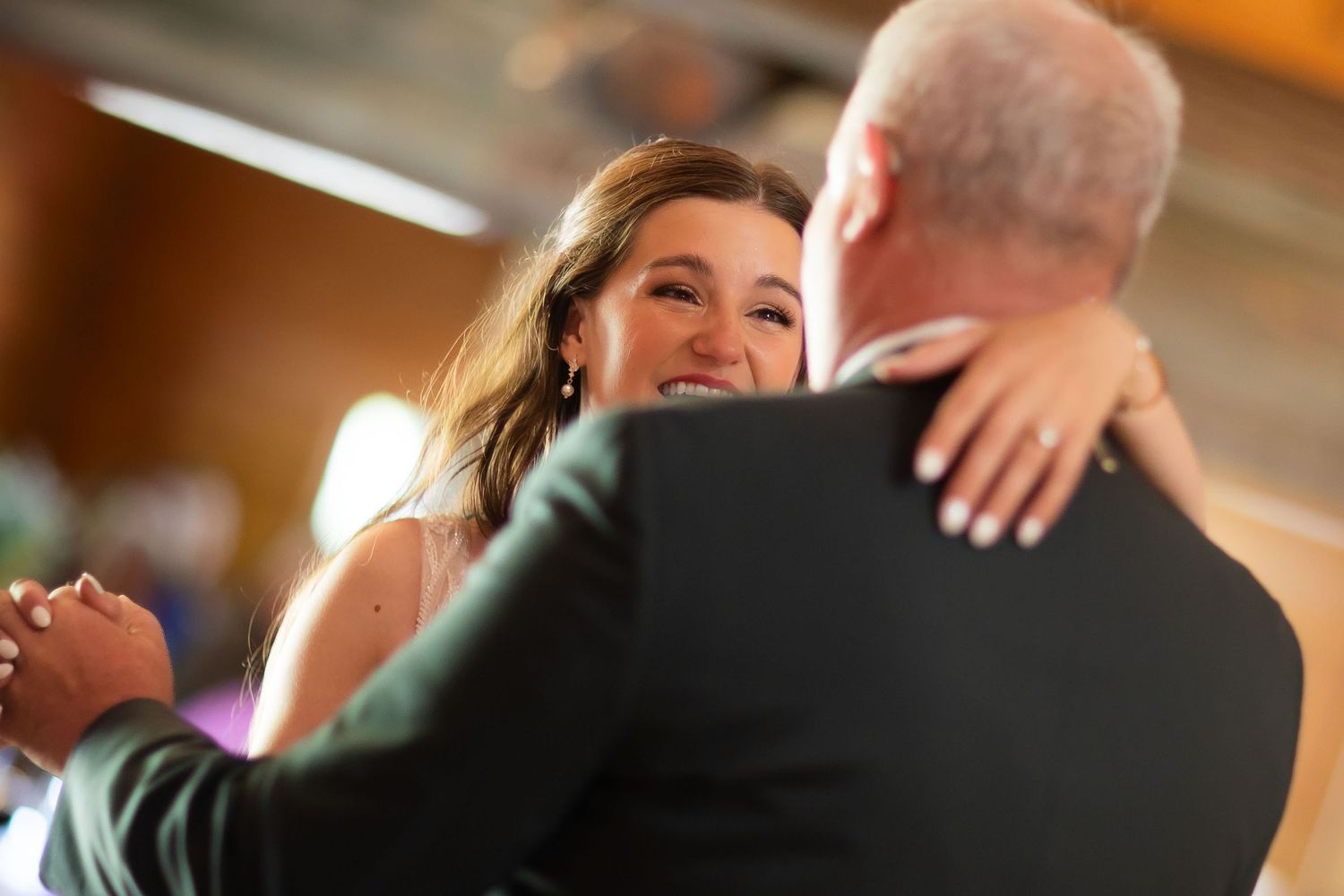 Smiling bride gazes at groom while sharing a romantic dance at their wedding reception.