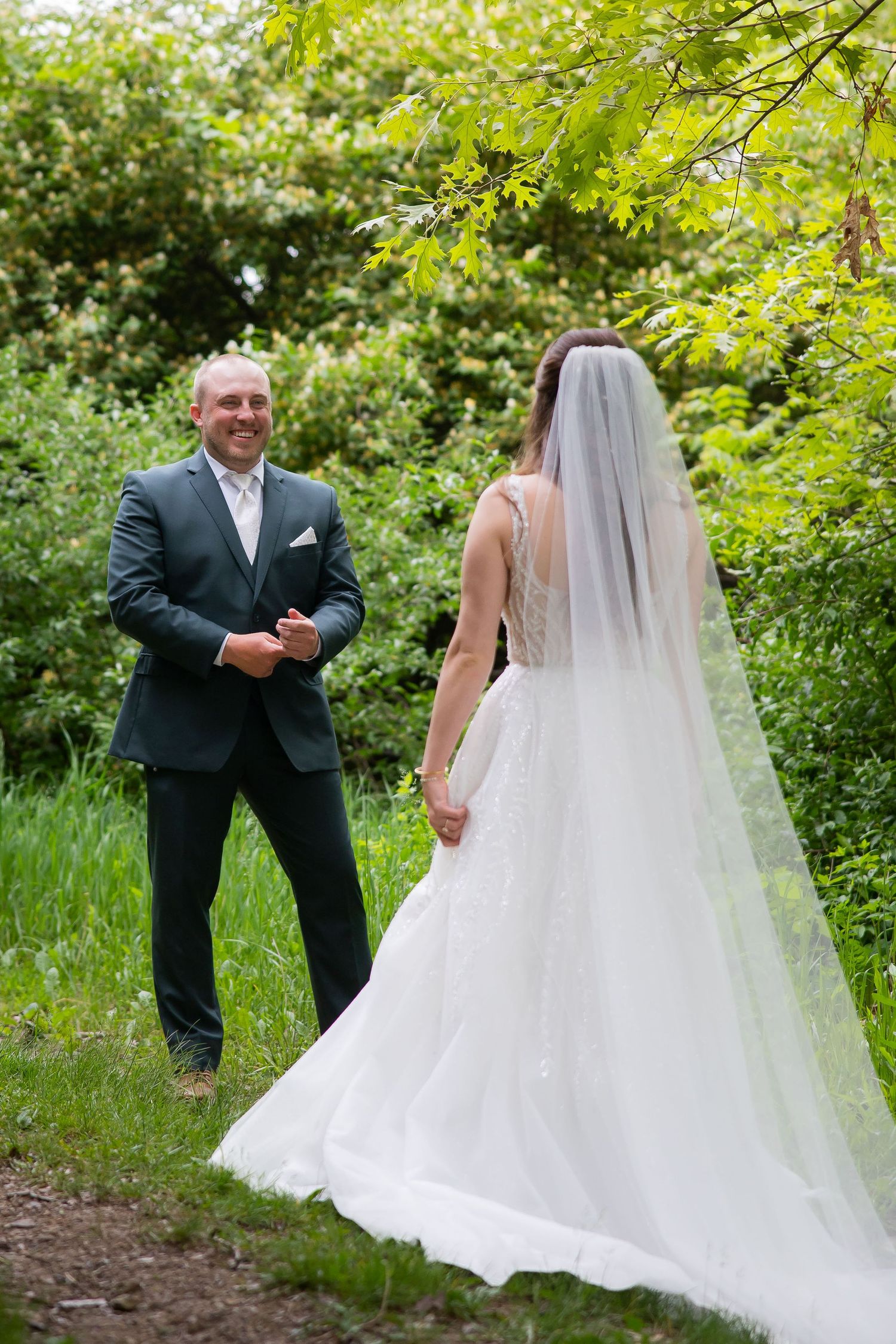 Groom smiling at bride during outdoor first look in lush green garden setting.