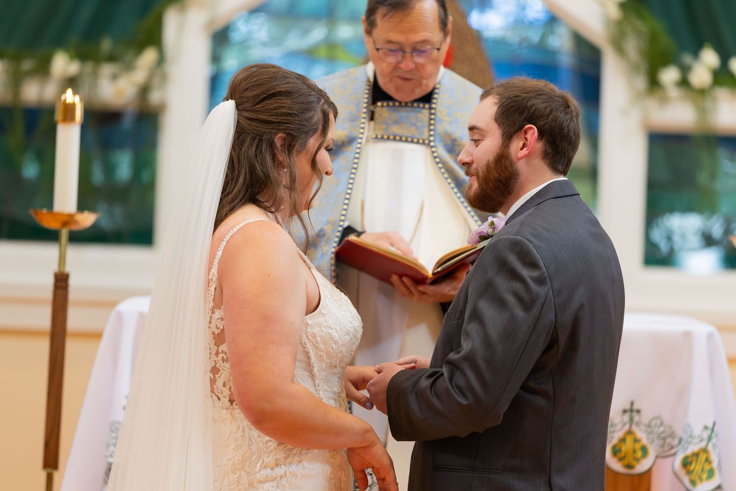Bride and groom exchanging vows during wedding ceremony with officiant holding book at church altar.