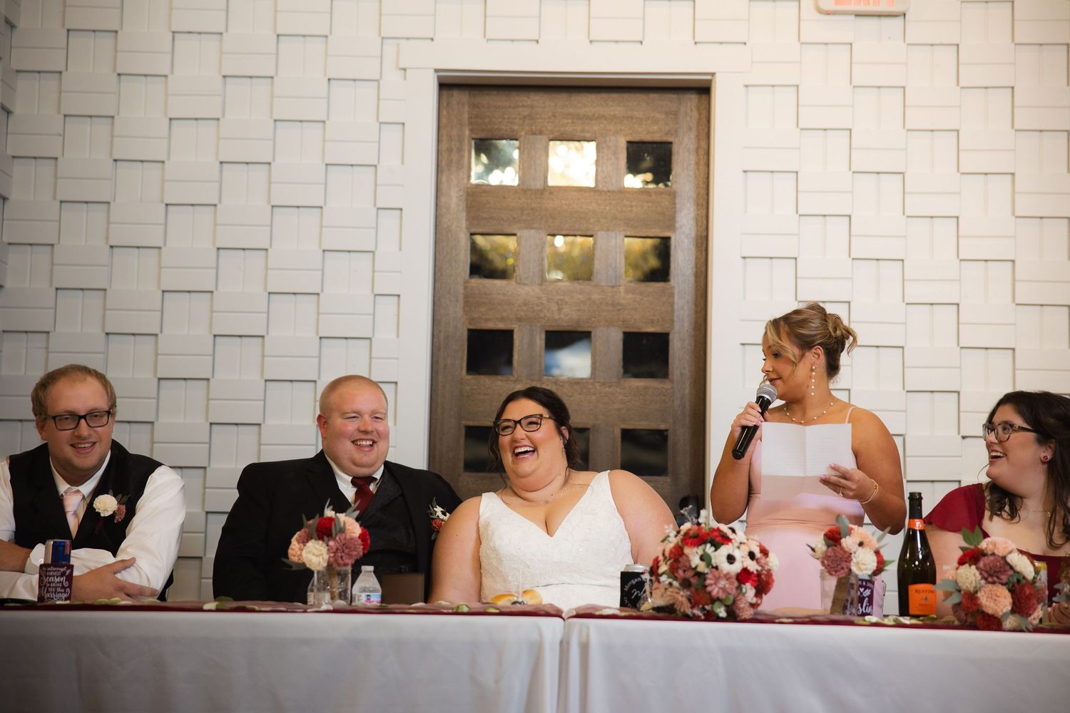 Wedding reception head table against textured white wall with decorative elements.