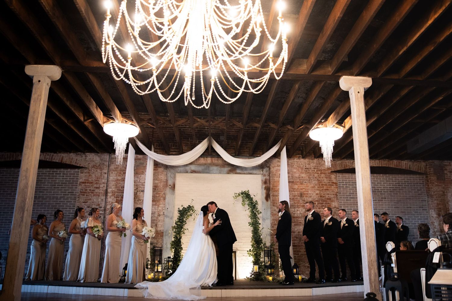 Elegant wedding ceremony setup with white chandeliers and brick walls creating a romantic atmosphere.