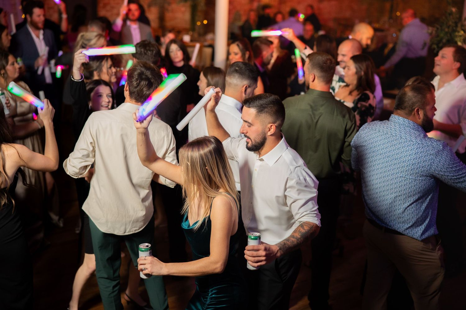 Energetic crowd dancing at wedding reception with colorful party lighting.