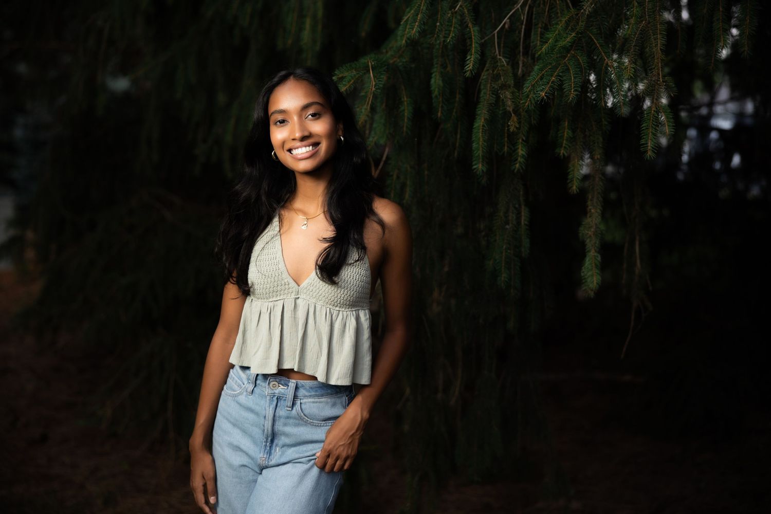 Person in ruffled top poses against dark foliage background.