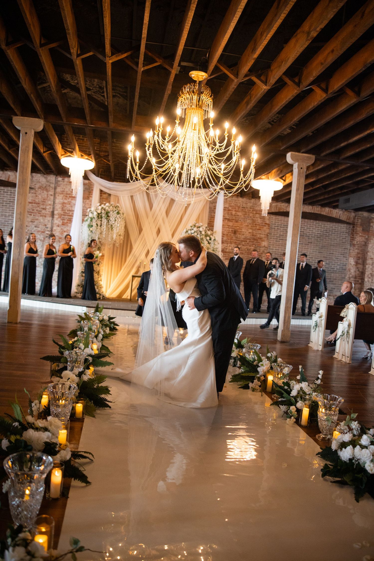 Elegant wedding venue with exposed brick walls, chandeliers and white drapery.