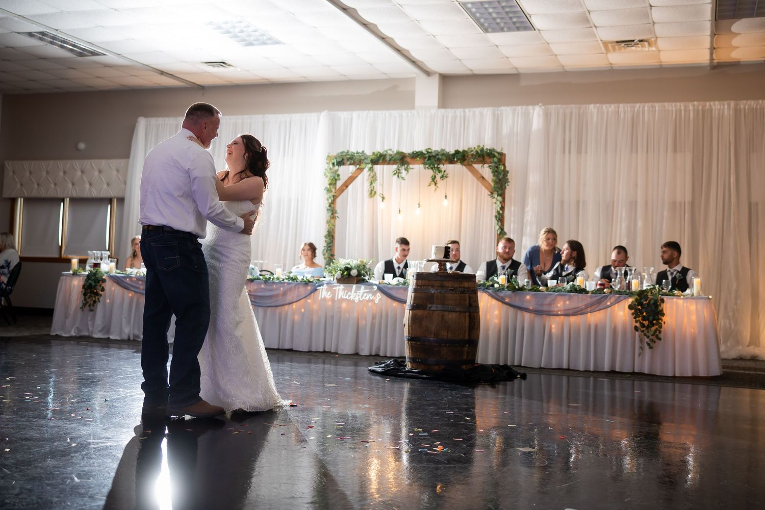 Bride and groom share first dance before floral arch at wedding reception.