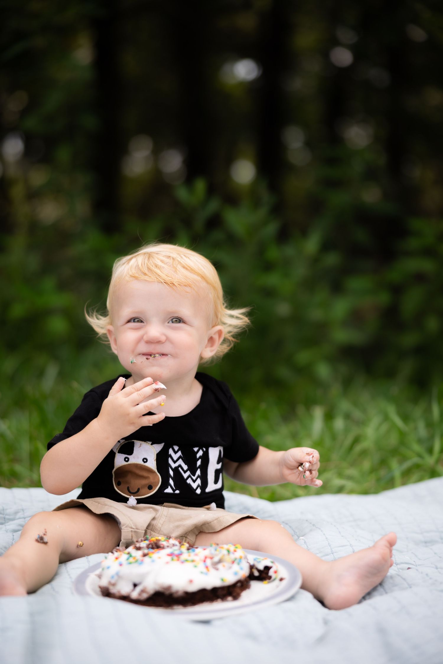 Child enjoying cake and sprinkles during outdoor first birthday photoshoot.