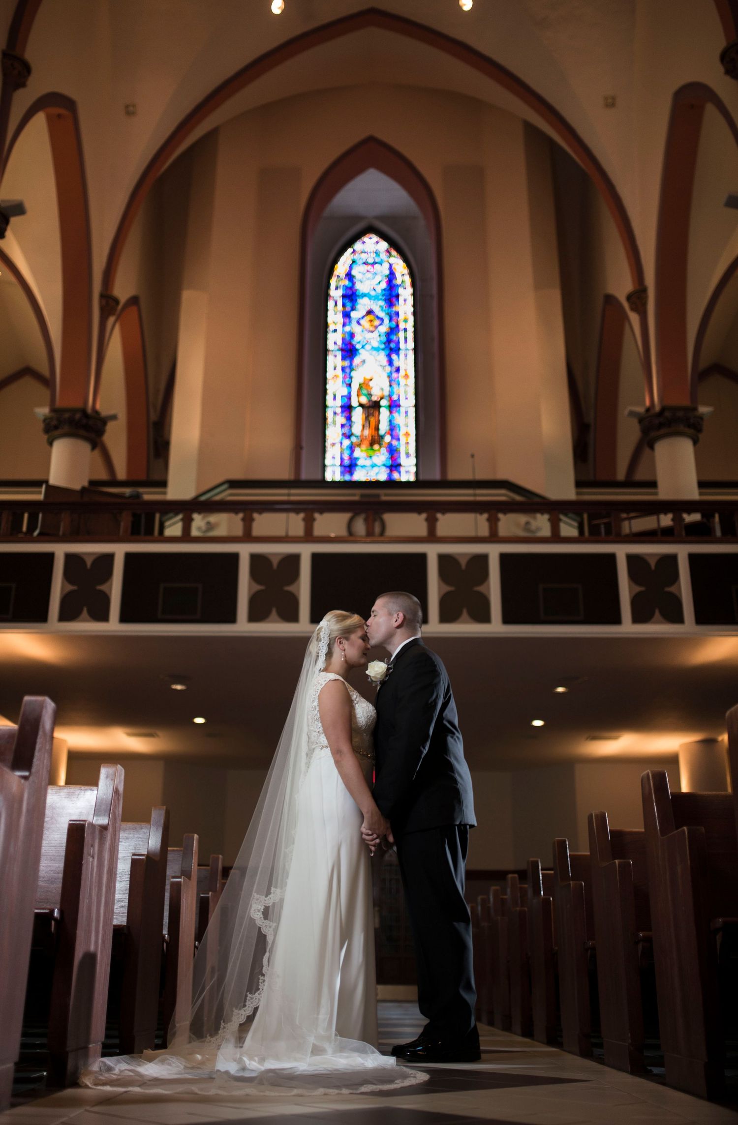 A couple stands in a beautiful church sanctuary with stained glass windows and wooden pews.