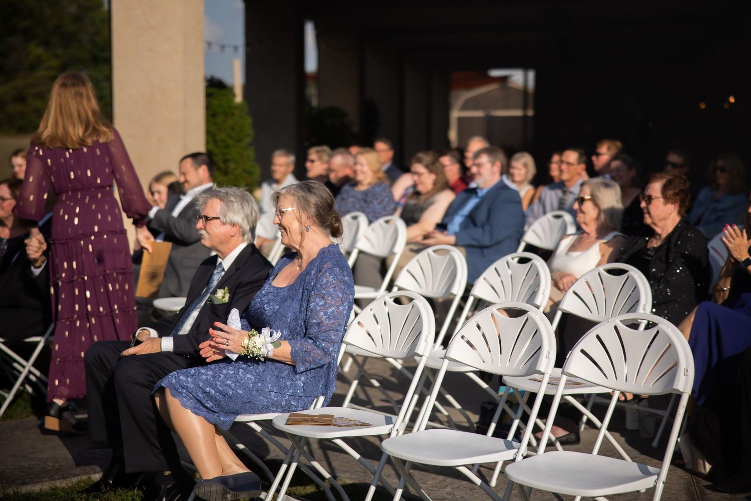 Wedding ceremony setup with white chairs and guests seated outdoors at sunset.