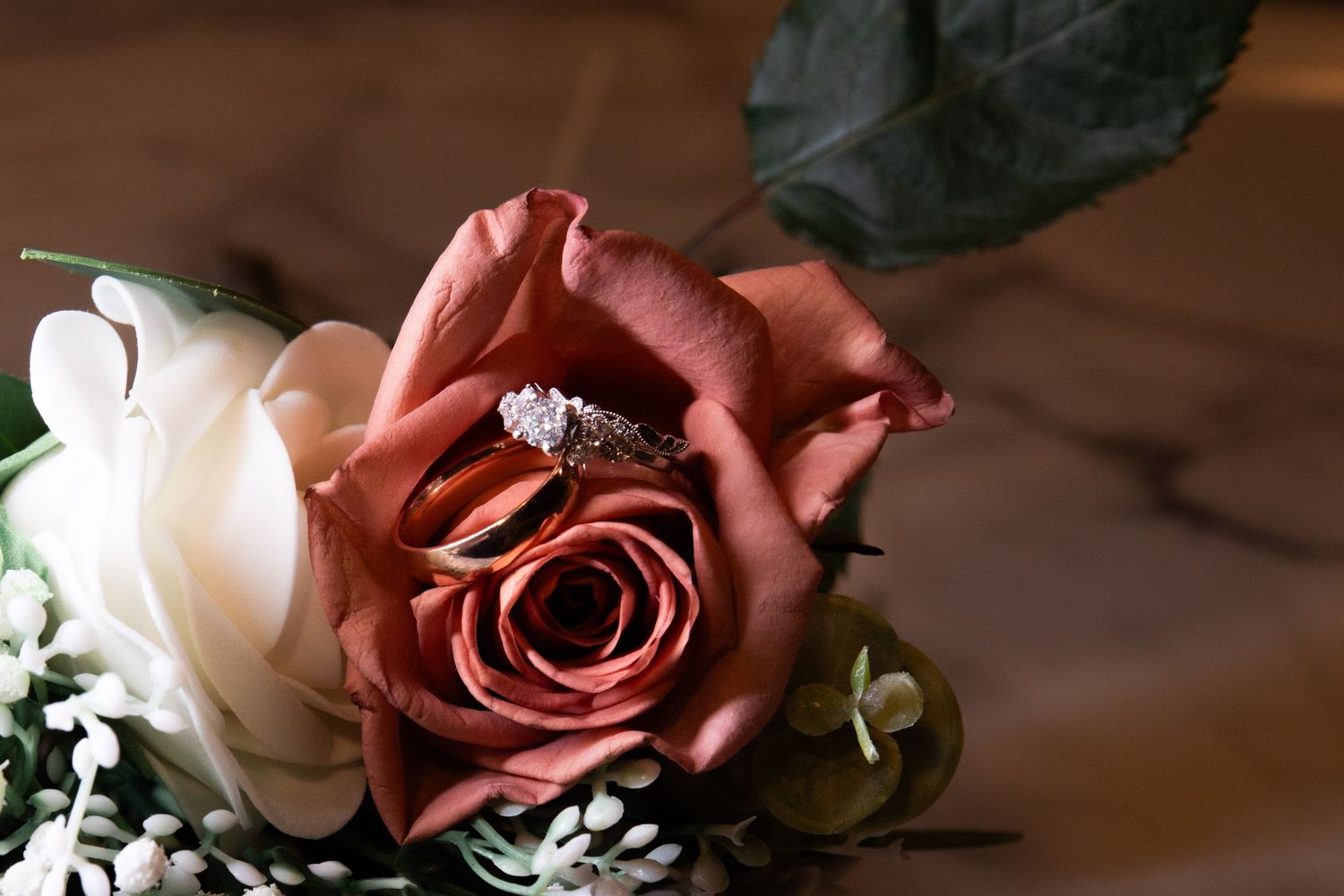 Diamond engagement ring resting inside a blooming dusty rose and white wedding bouquet.