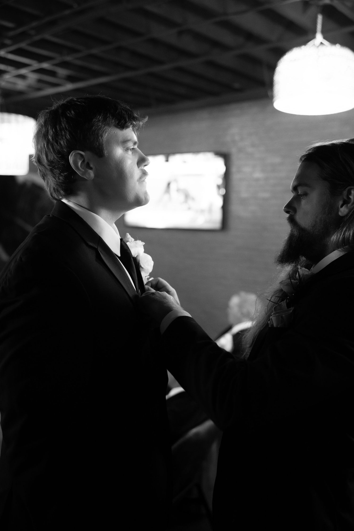 Two people in dark formal attire share an intimate moment in a dimly lit room.