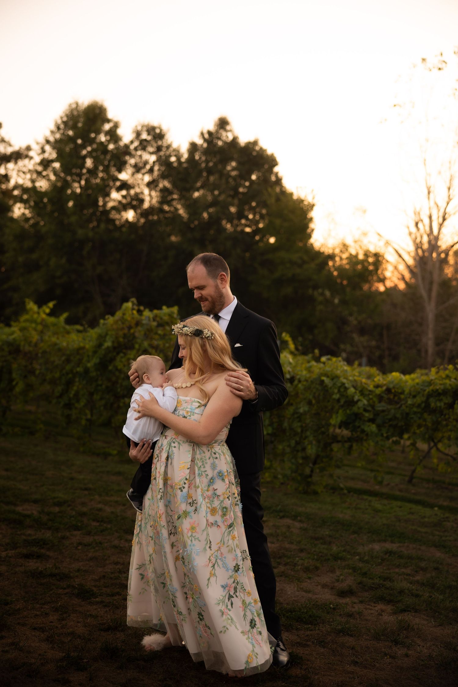 A couple dances together in a vineyard at sunset with soft golden light filtering through the trees.