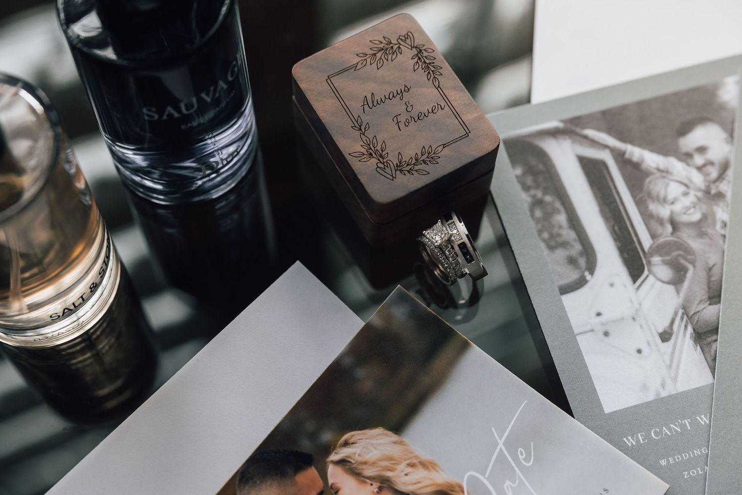 Wedding details including a wooden ring box, wine bottle, and black and white photographs arranged on a surface.
