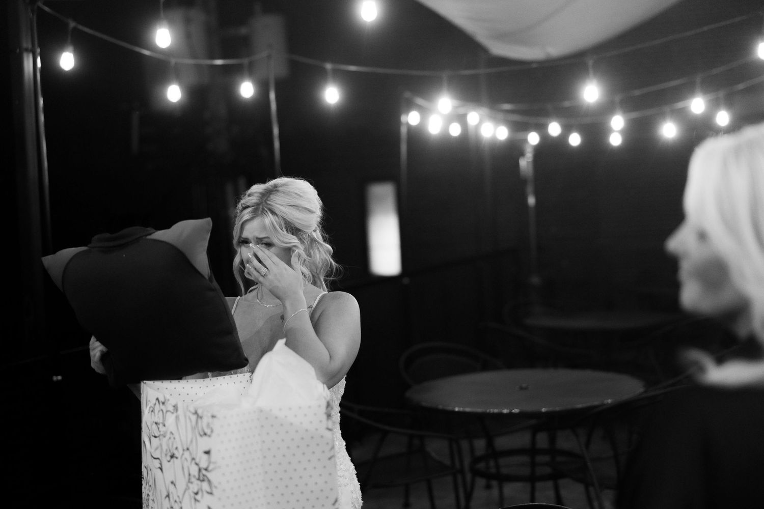 Black and white emotional moment captured during wedding reception under string lights.