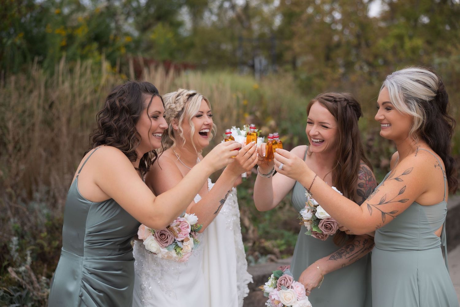 Bridesmaids in sage green dresses share laughs and drinks with the bride during wedding celebrations.