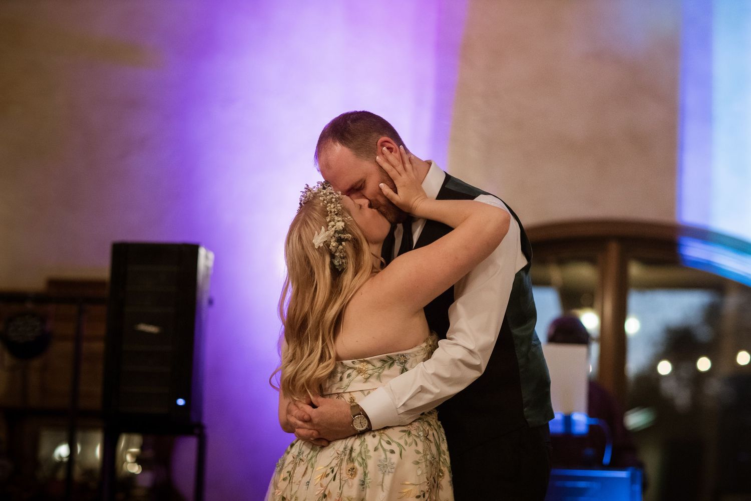 A couple shares a romantic dance moment under purple lighting at their wedding reception.