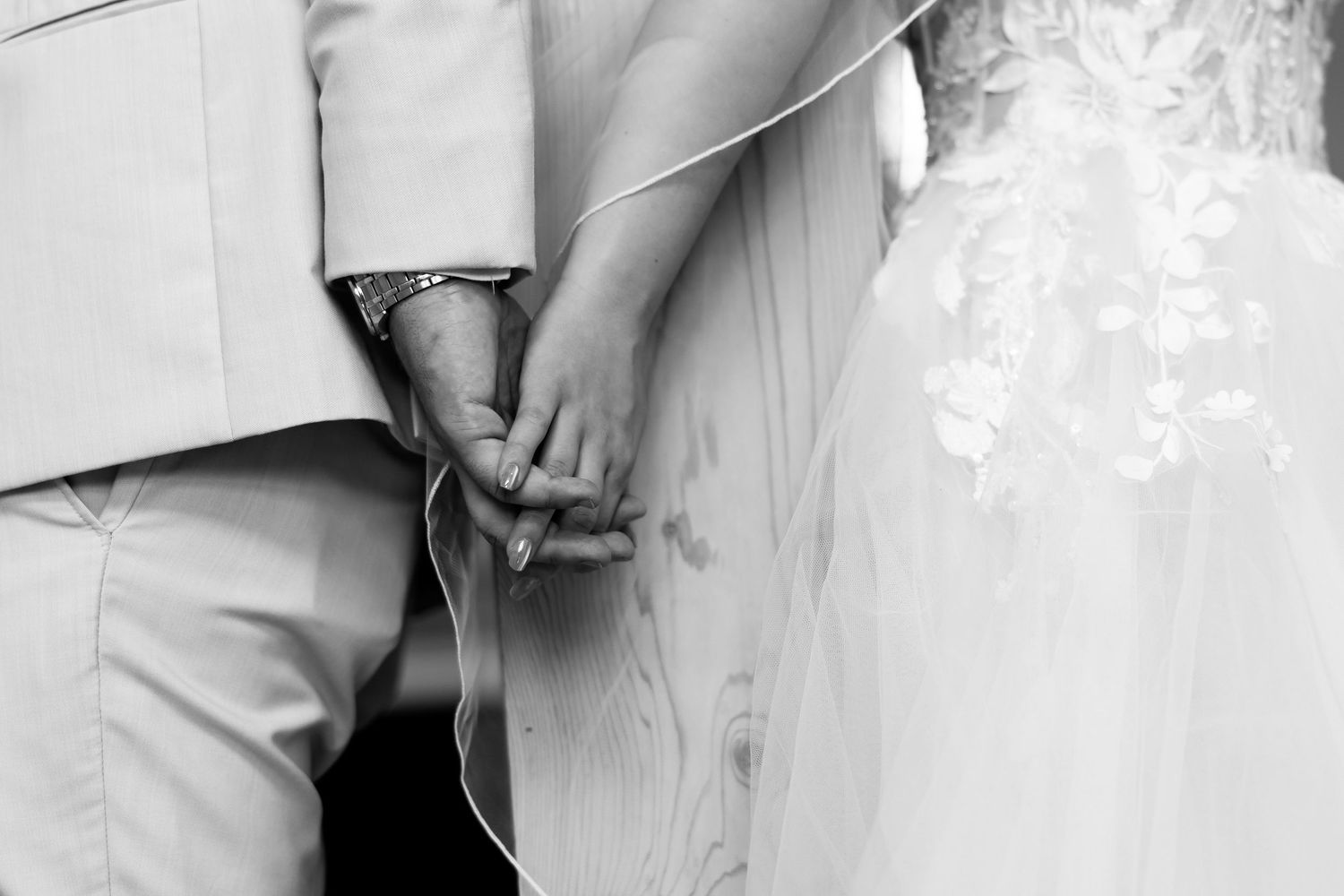 Black and white photo of bride and groom holding hands at wedding ceremony.