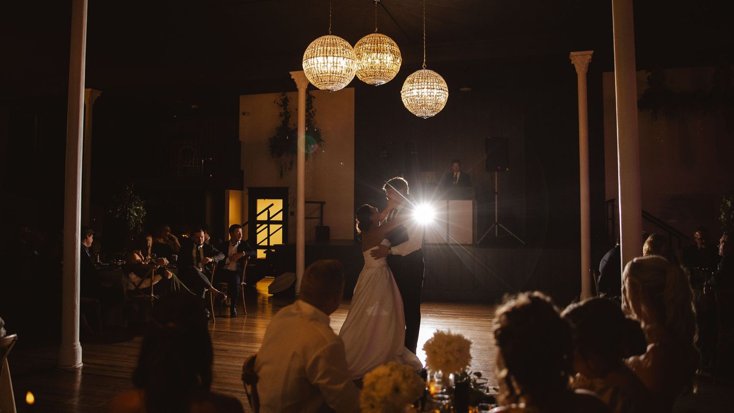 Silhouetted first dance at wedding reception with glowing pendant lights overhead.