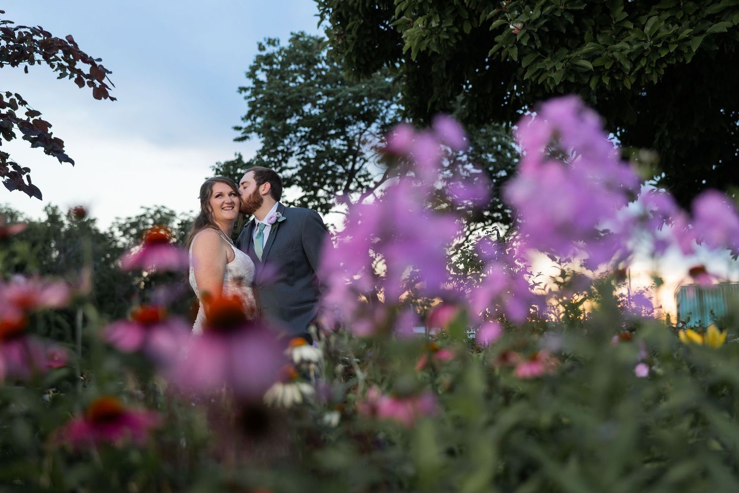 Couple embracing in a lush garden with purple coneflowers in foreground at dusk.