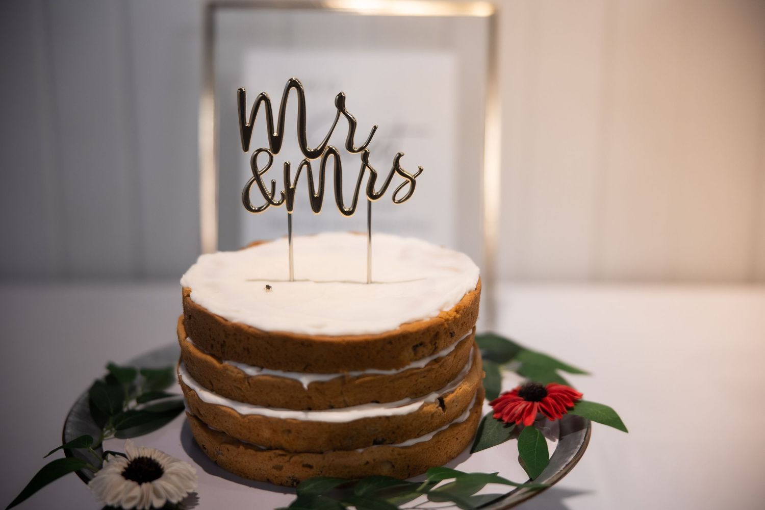 Wedding cake decorated with a 'Mr & Mrs' topper and floral accents sits elegantly on display.