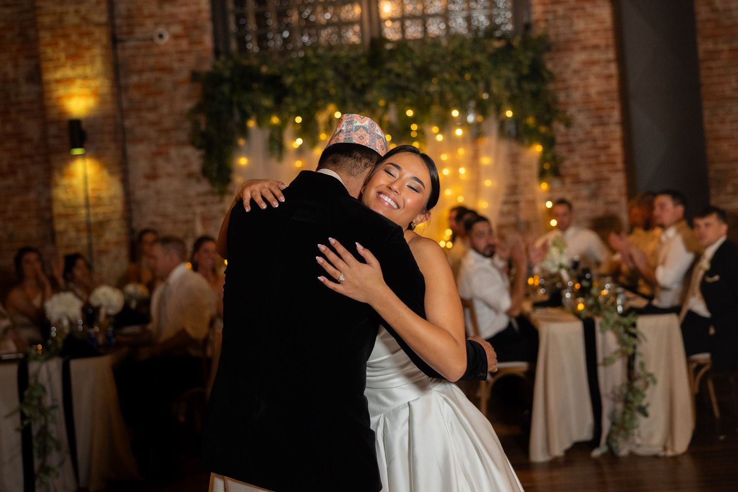 Couple sharing romantic dance at wedding reception with brick walls and warm lighting.