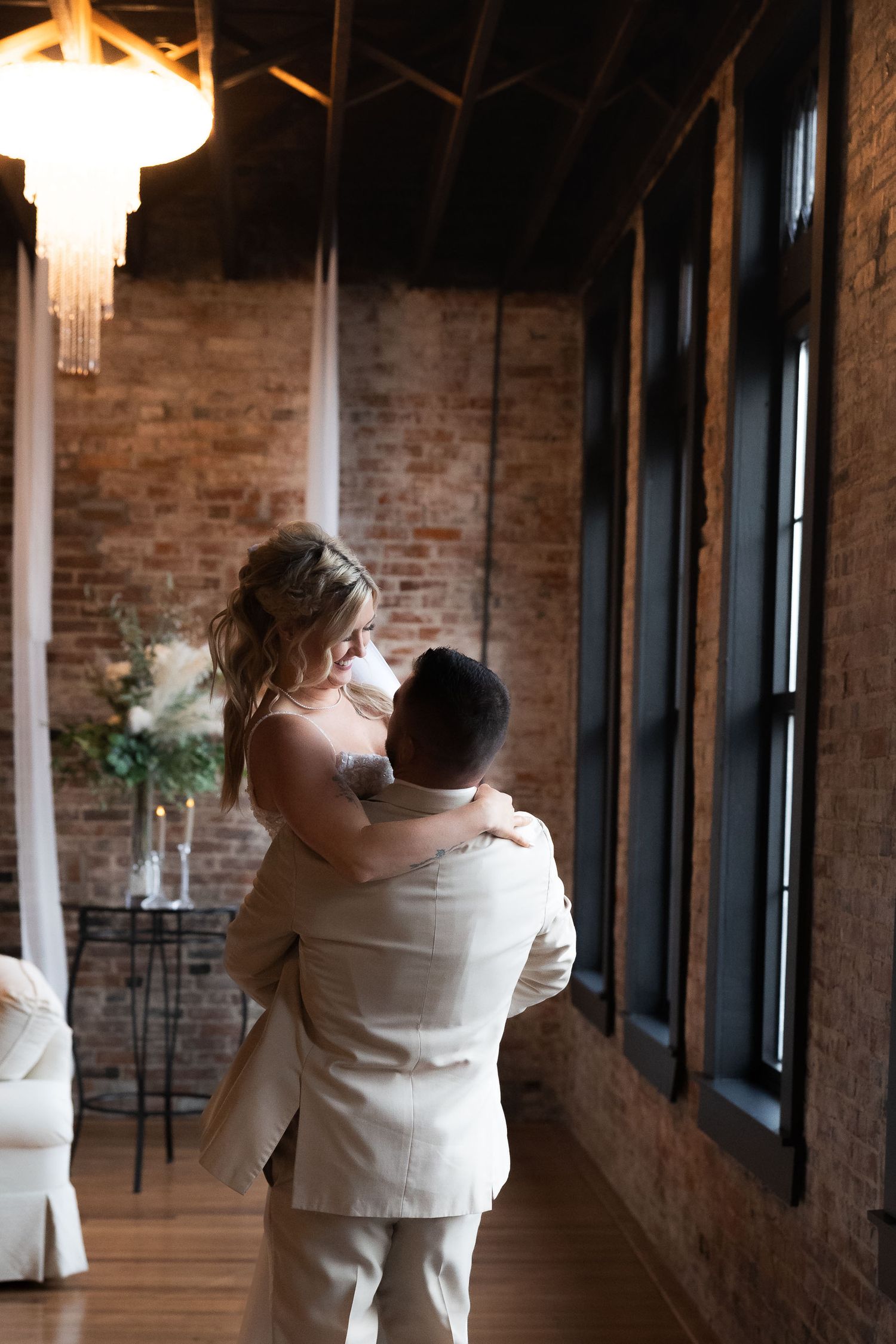 Couple dancing together in an elegant brick-walled venue with crystal chandeliers overhead.