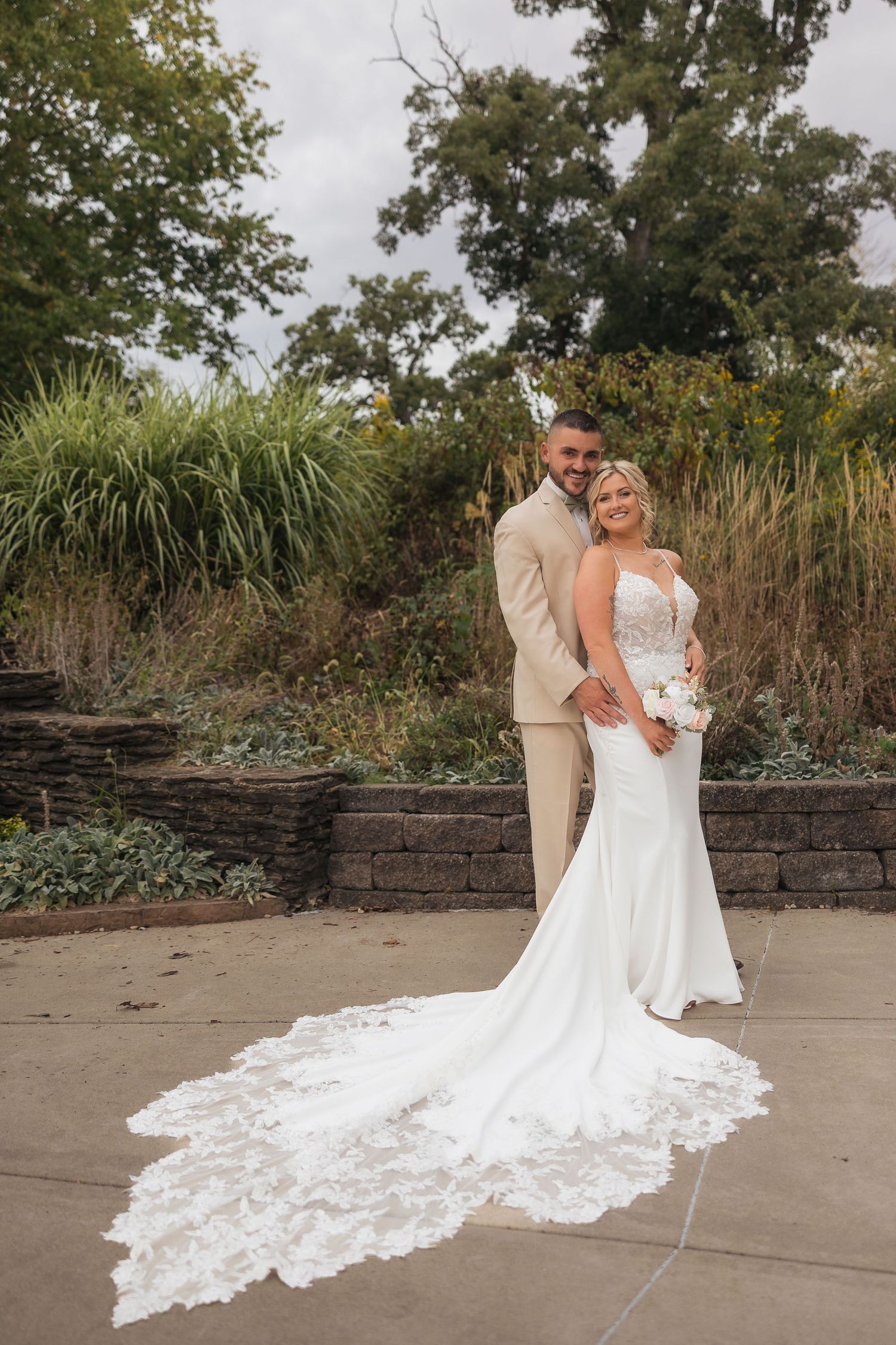 Elegant wedding photo showcasing bride's long lace train against outdoor garden setting.