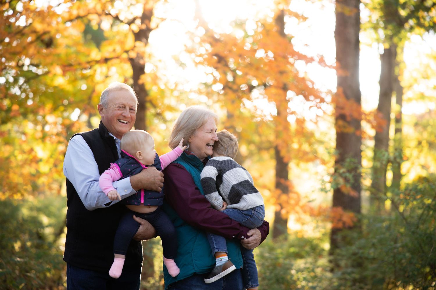 Family members embrace and laugh together in autumn forest setting with golden light.