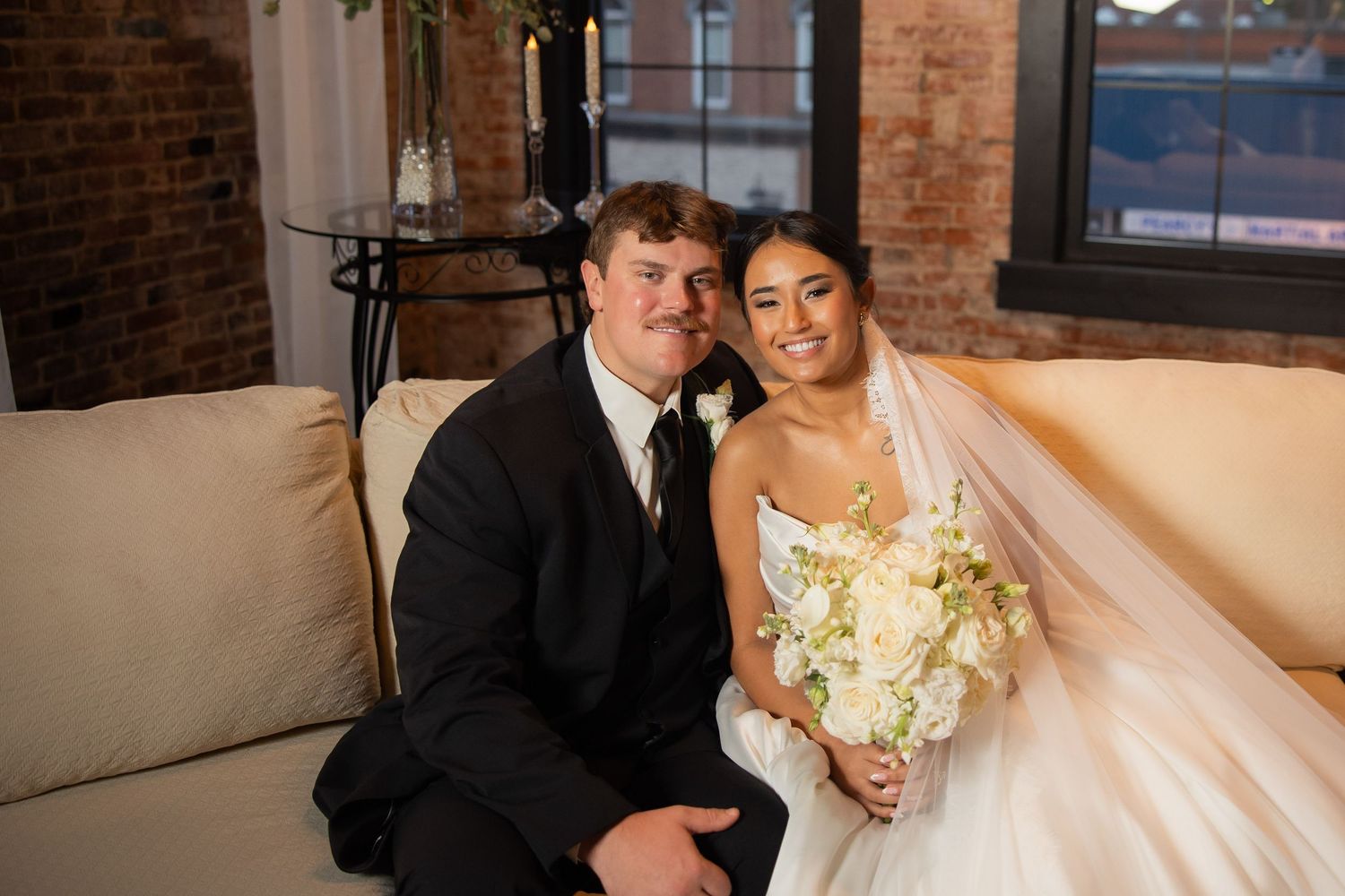 A wedding couple shares a tender moment in front of exposed brick walls and natural lighting.