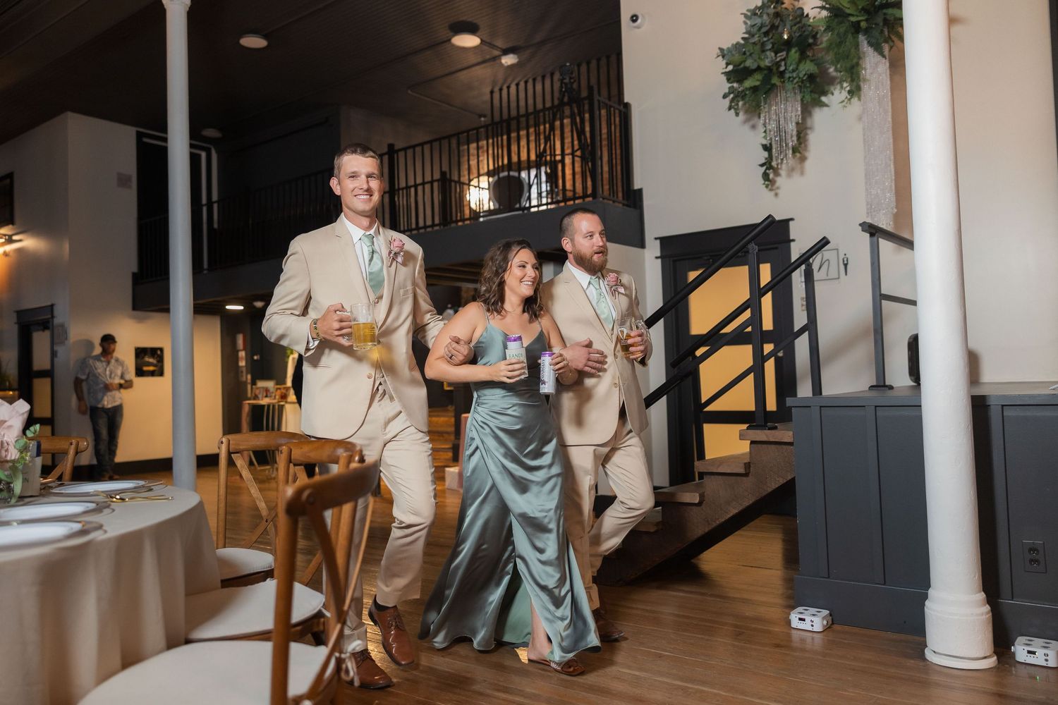 Wedding guests dance and celebrate under elegant chandeliers in an industrial-chic venue with exposed brick walls.