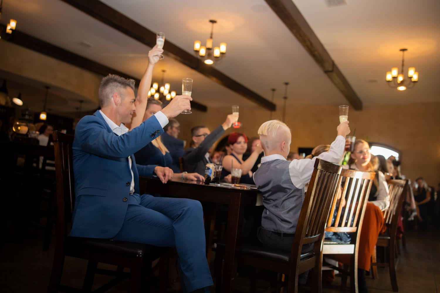 Wedding guests mingle and celebrate in an elegant indoor reception venue with warm lighting and chandeliers.