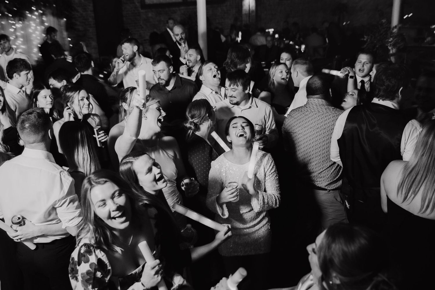 Wedding guests dancing and celebrating on dimly lit dance floor.