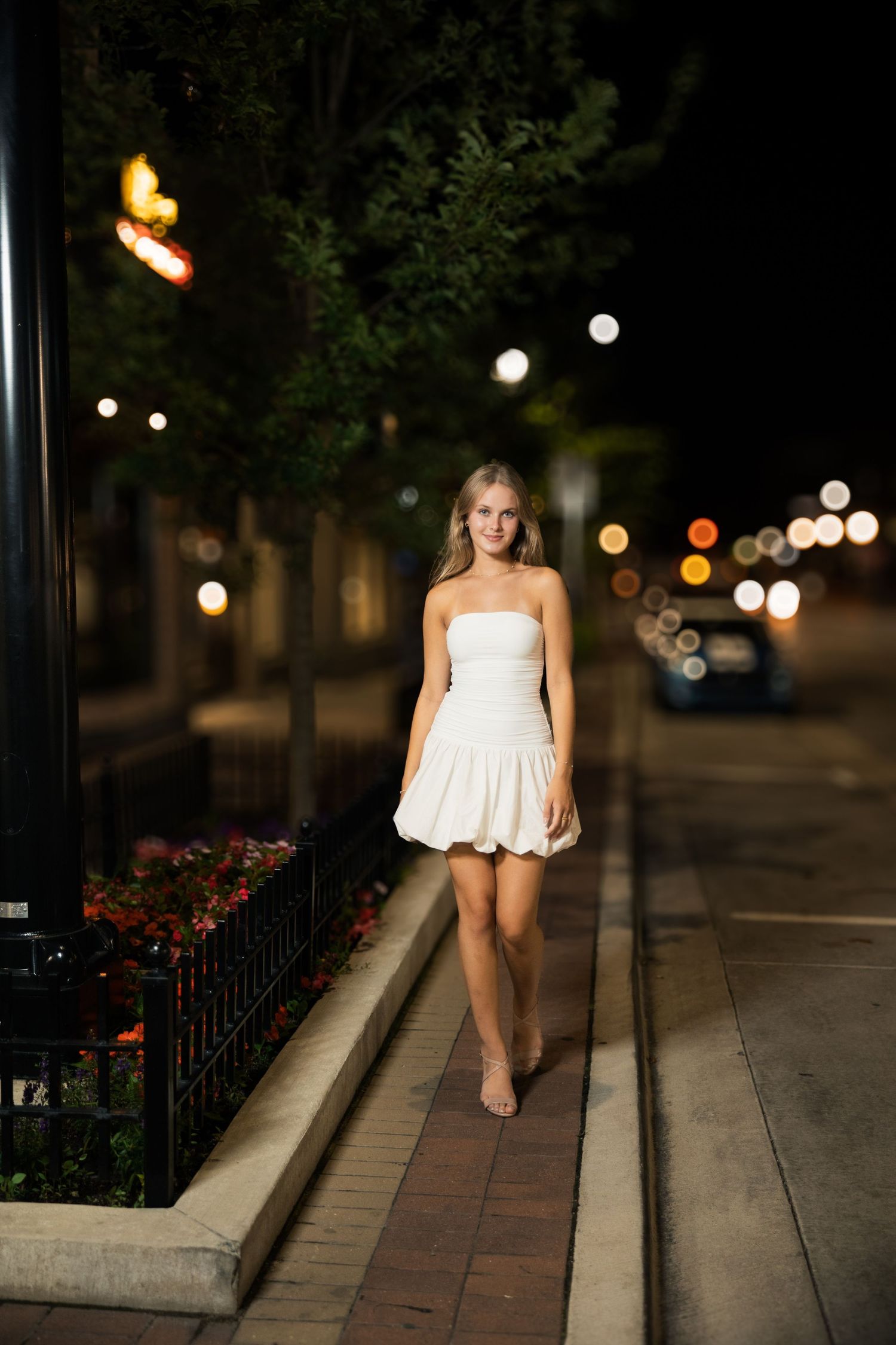 A white summer dress photographed at night along a path with bokeh lights in the background.