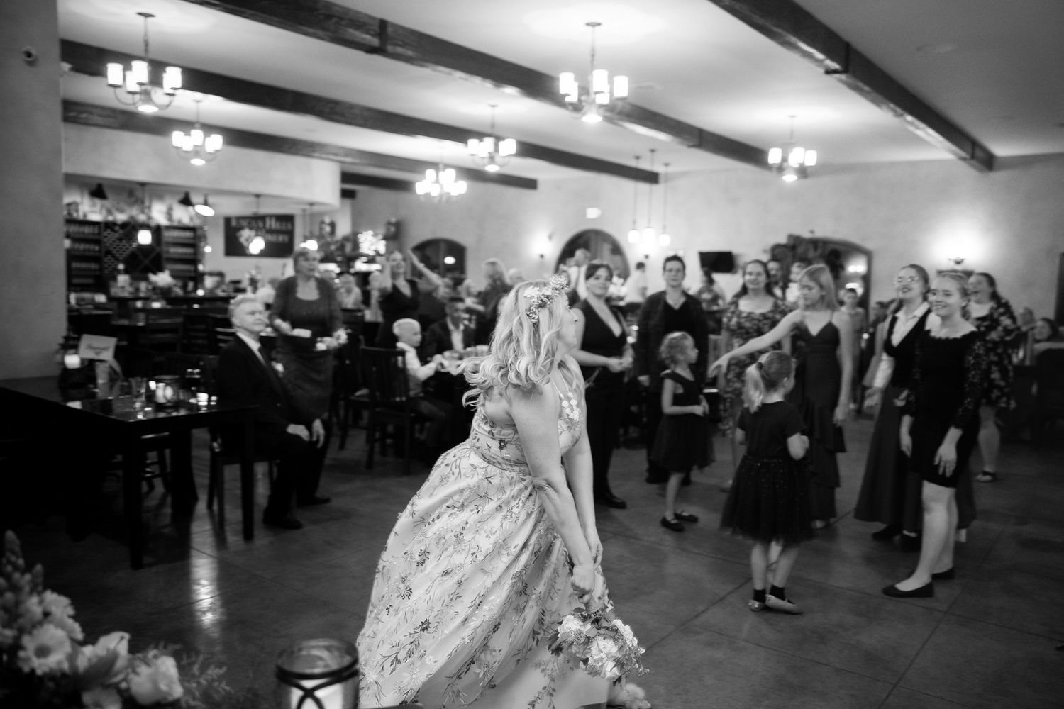 A black and white photo shows wedding guests watching a couple dance at their reception.